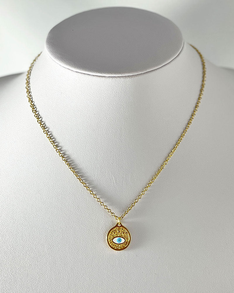 A dainty chain necklace with a small round pendant. The pendant is gold with a white blue enamel evil eye design.