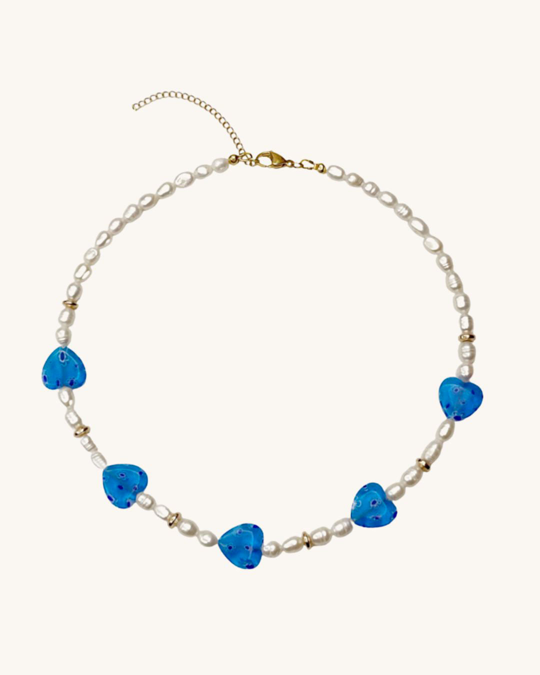 A white pearl necklace with five blue heart-shaped glass beads. The hearts have a white floral pattern on them.
