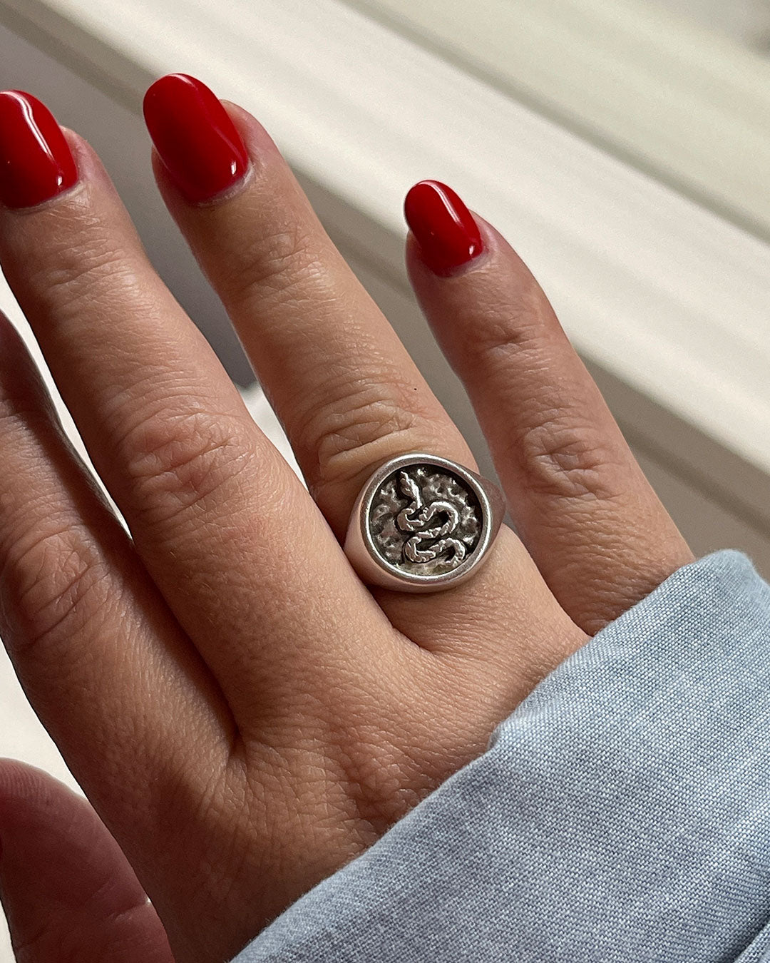 A close-up image of a person's finger wearing a silver ring with a snake design.