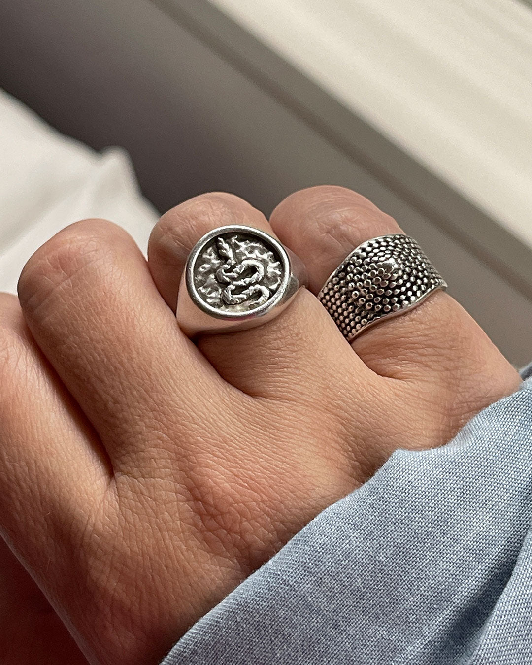 A snake stamp ring and a silver dot ring with a textured design on a finger.