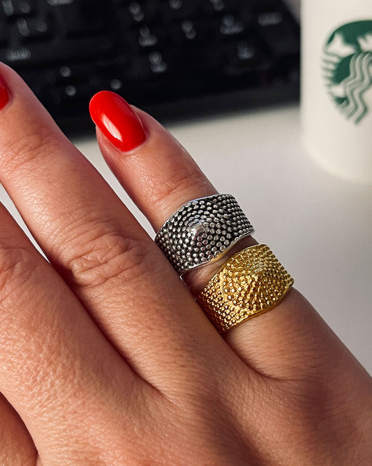 A silver and a gold ring with a textured design on a finger. The ring has a small dot pattern and a conical center.