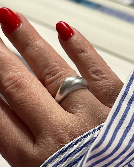 A silver, slightly adjustable wave ring worn on a person's finger