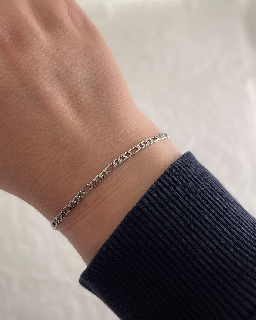 Wrist with a delicate Figaro chain bracelet in silver finish
