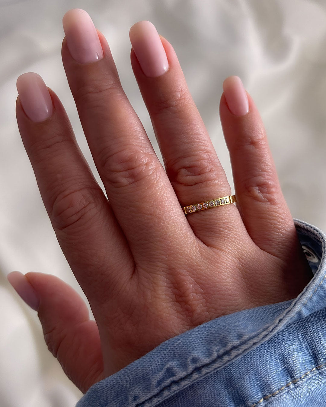 A woman’s hand wearing a gold band ring with diamonds on a neutral background