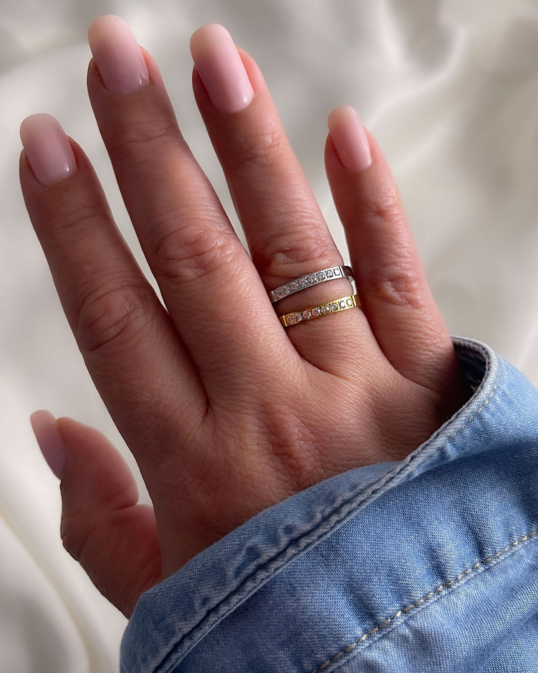 A woman’s hand wearing gold & silver band rings with diamonds on a neutral background