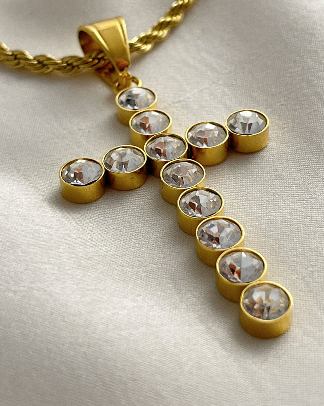 A gold chain necklace with a gold cross pendant. The cross is adorned with clear round crystals.