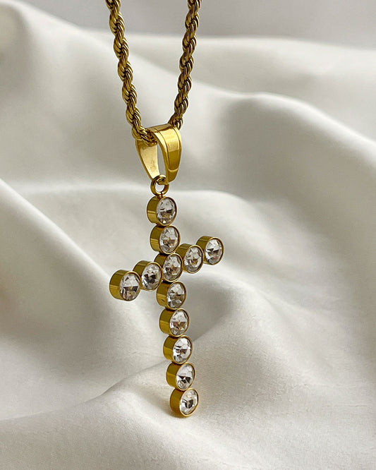A gold chain necklace with a gold cross pendant. The cross is adorned with clear round crystals.