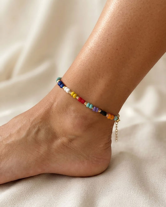 A colorful glass beaded anklet adorned with gold metal beads on a foot