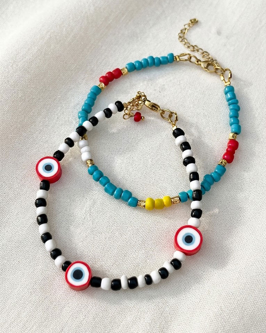 A Rainbow Beaded Summer Anklet adorned with gold metal beads and a black & white beaded anklet with red evil eye beads