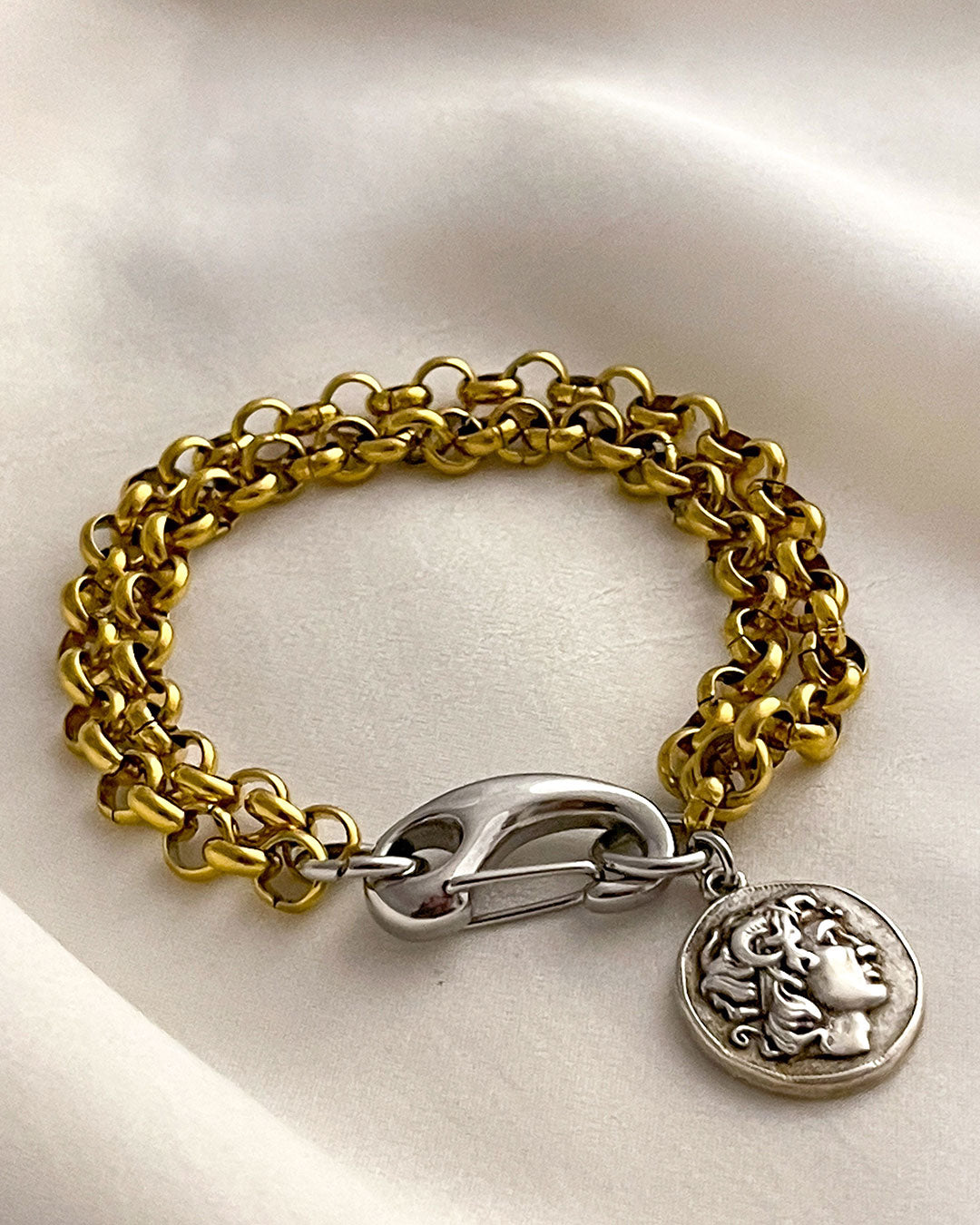 Gold chain bracelet with a silver clasp and a double side coin charm on a white background