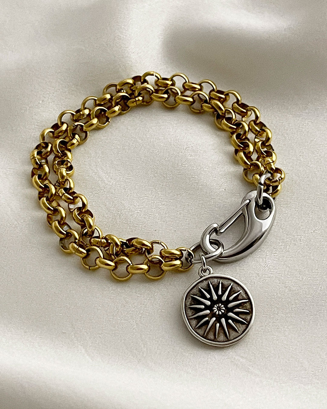 Gold chain bracelet with a silver clasp and a double side coin charm on a white background