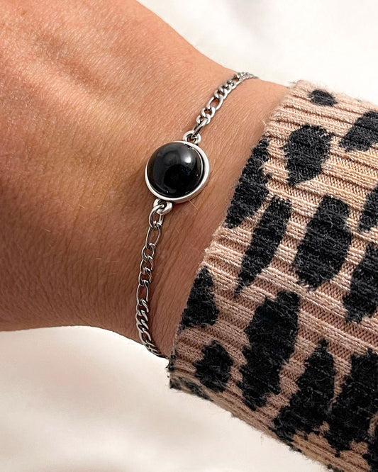 Silver figaro chain bracelet with a black onyx stone on a wrist wearing a leopard print sleeve.