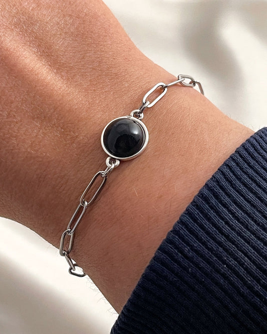 Silver paperclip chain bracelet with a black onyx stone on a wrist against a neutral background