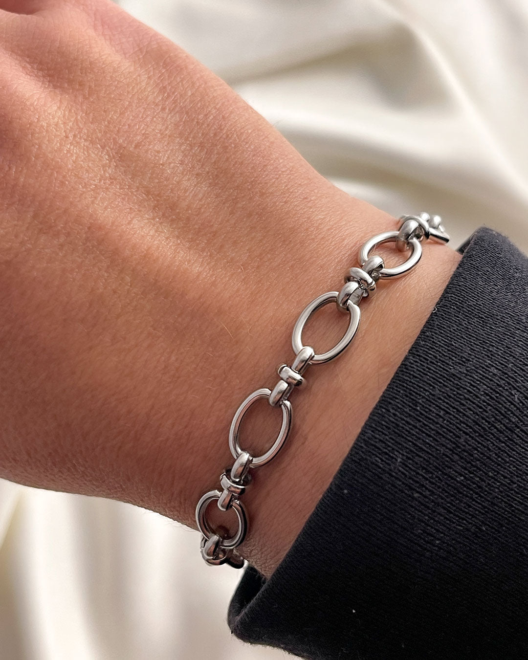 Silver oval link chain bracelet on a wrist with a neutral background