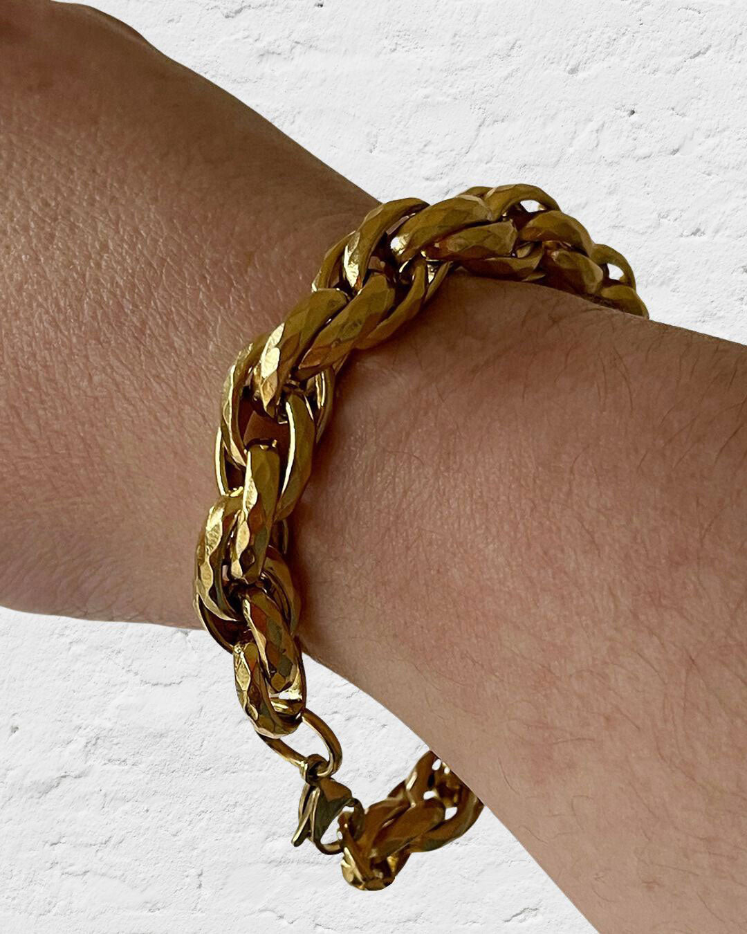 Gold chunky braided chain bracelet on a wrist against a white background