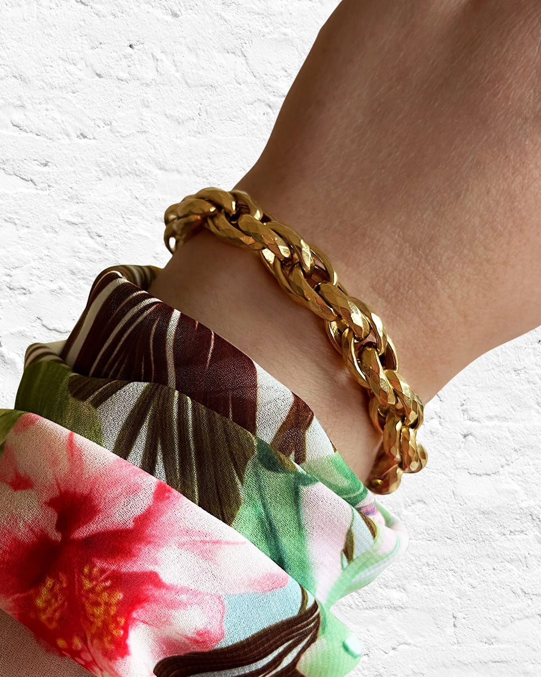 Gold chunky braided chain bracelet on a wrist against a white background