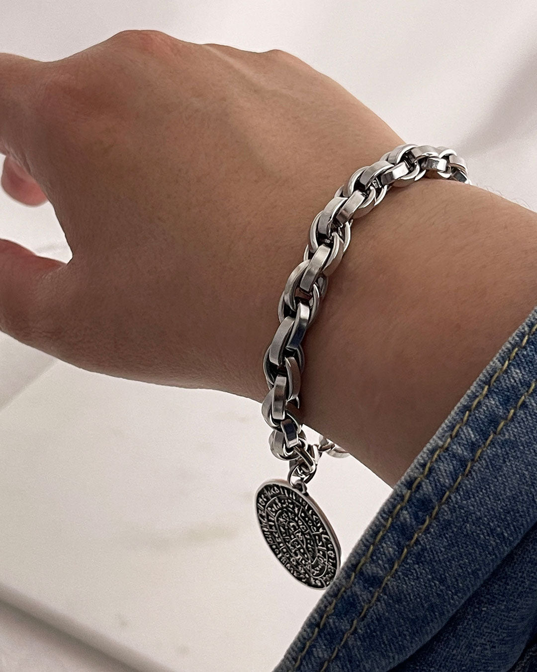 Silver bracelet on the wrist with a round Phaistos disc, against a neutral background