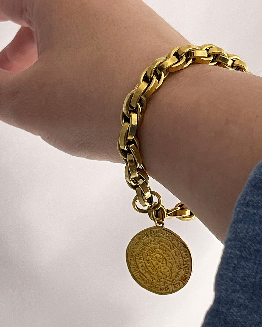 Gold bracelet on the wrist with a round Phaistos disc, against a neutral background