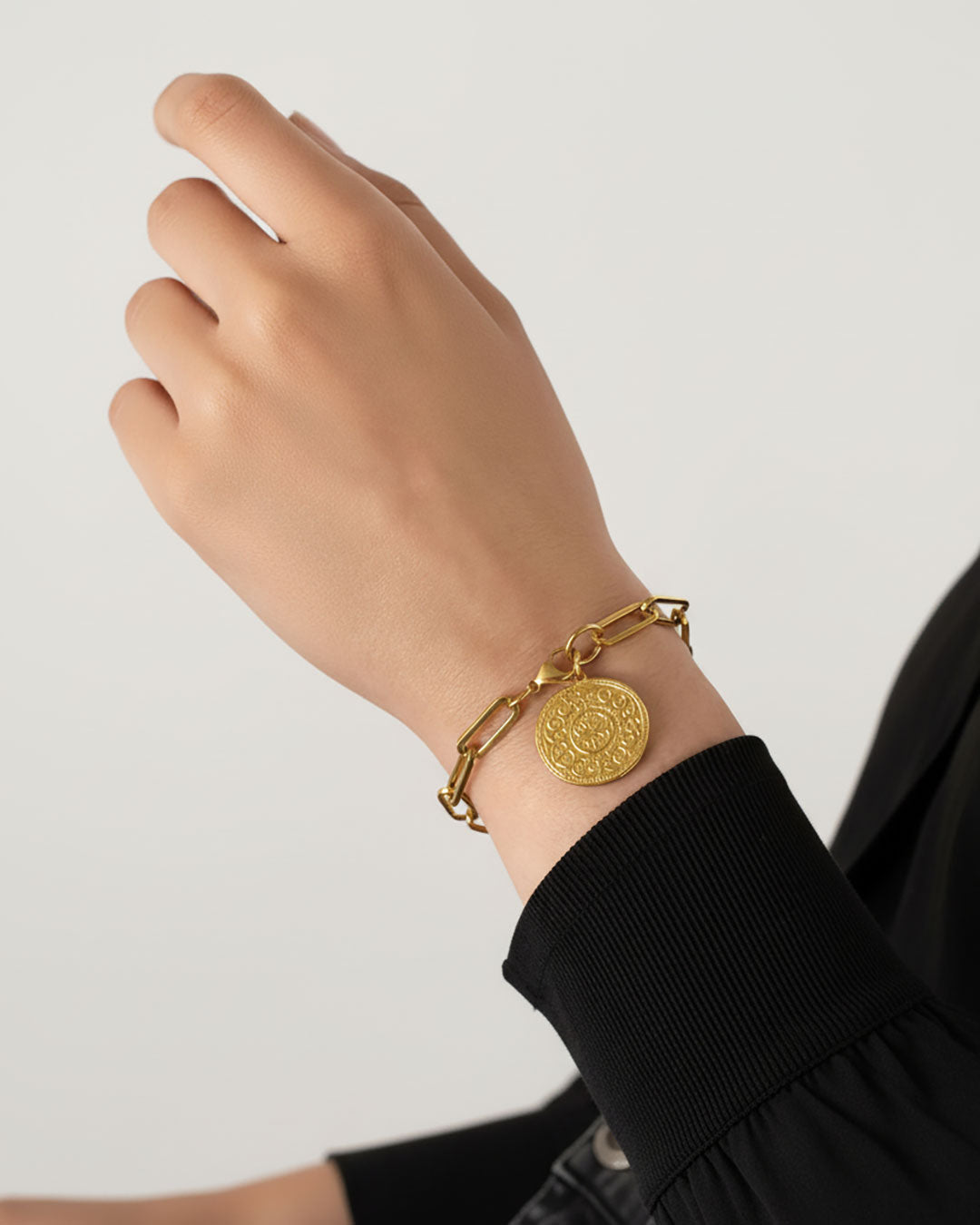 Gold bracelet with a decorative coin charm on a wrist against a neutral background