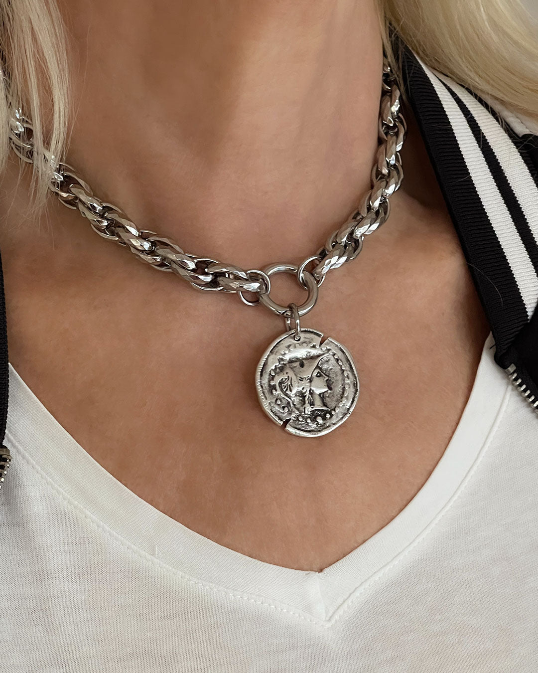 Model wearing a silver tone chunky chain necklace with a large coin pendant. The coin features an embossed profile of a woman's face. The necklace is a bold statement piece with a substantial chain and a detailed pendant. The chain is thick and rope-like, and the pendant is substantial and eye-catching.