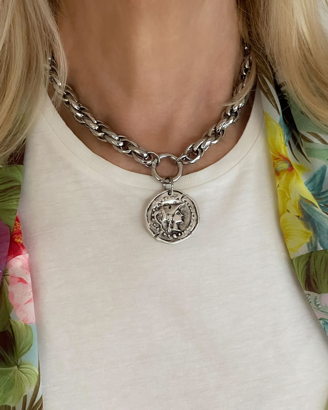 Model wearing a silver tone chunky chain necklace with a large coin pendant. The coin features an embossed profile of a woman's face. The necklace is a bold statement piece with a substantial chain and a detailed pendant. The chain is thick and rope-like, and the pendant is substantial and eye-catching.