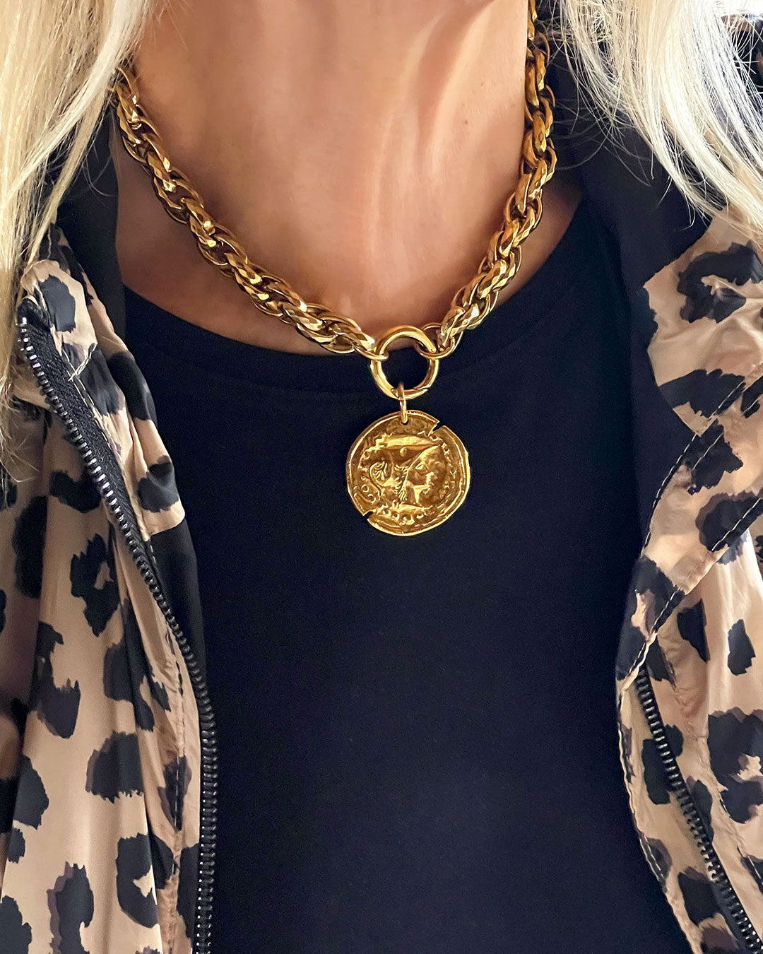 Model wearing a gold chunky chain necklace with a large coin pendant. The coin features an embossed profile of a woman's face. The necklace is a bold statement piece with a substantial chain and a detailed pendant.