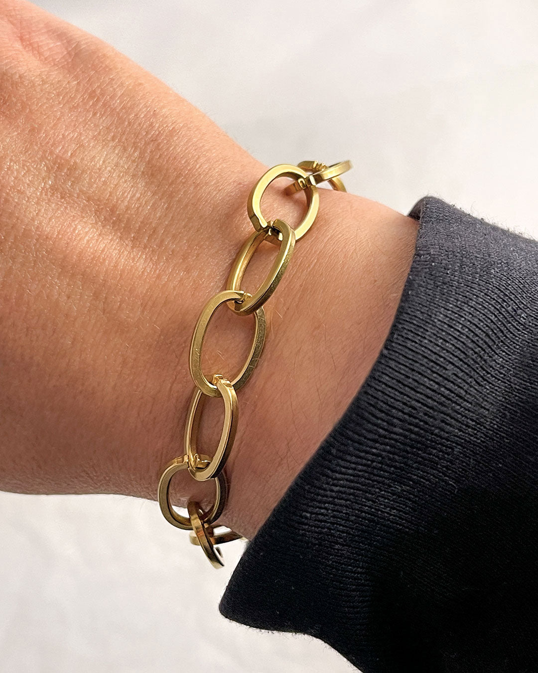 Chunky oval links chain bracelet in gold on a wrist with a plain background