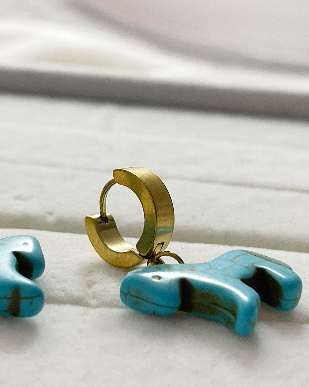 Turquoise horse-shaped earrings with gold hoops on a white surface