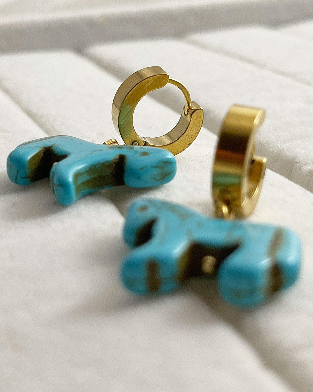 Turquoise horse-shaped earrings with gold hoops on a white surface