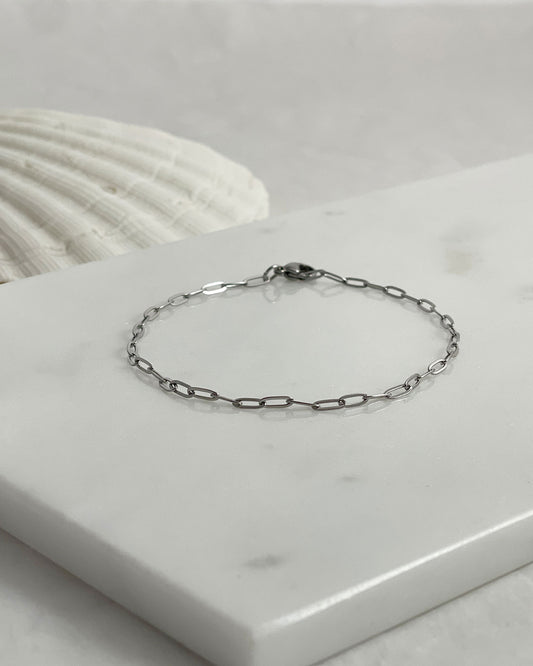 Silver paperclip chain bracelet on a marble surface with a shell in the background