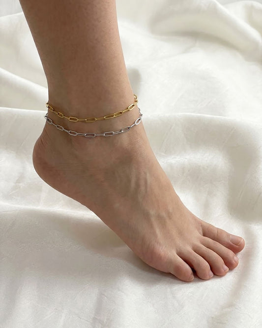 Two gold and silver paperclip chain amklets on a foot