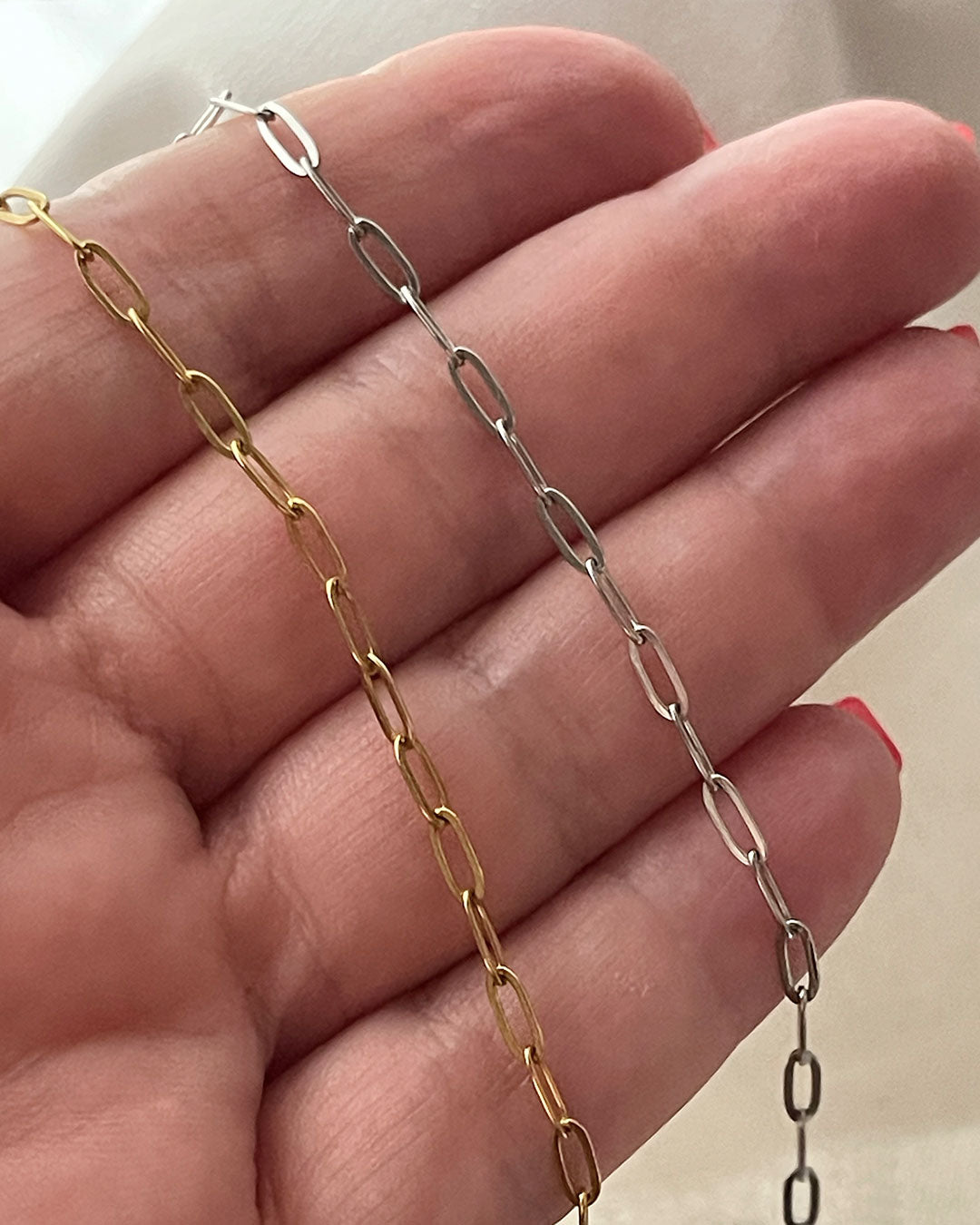 Two gold and silver paperclip chain necklaces on a hand against a neutral background