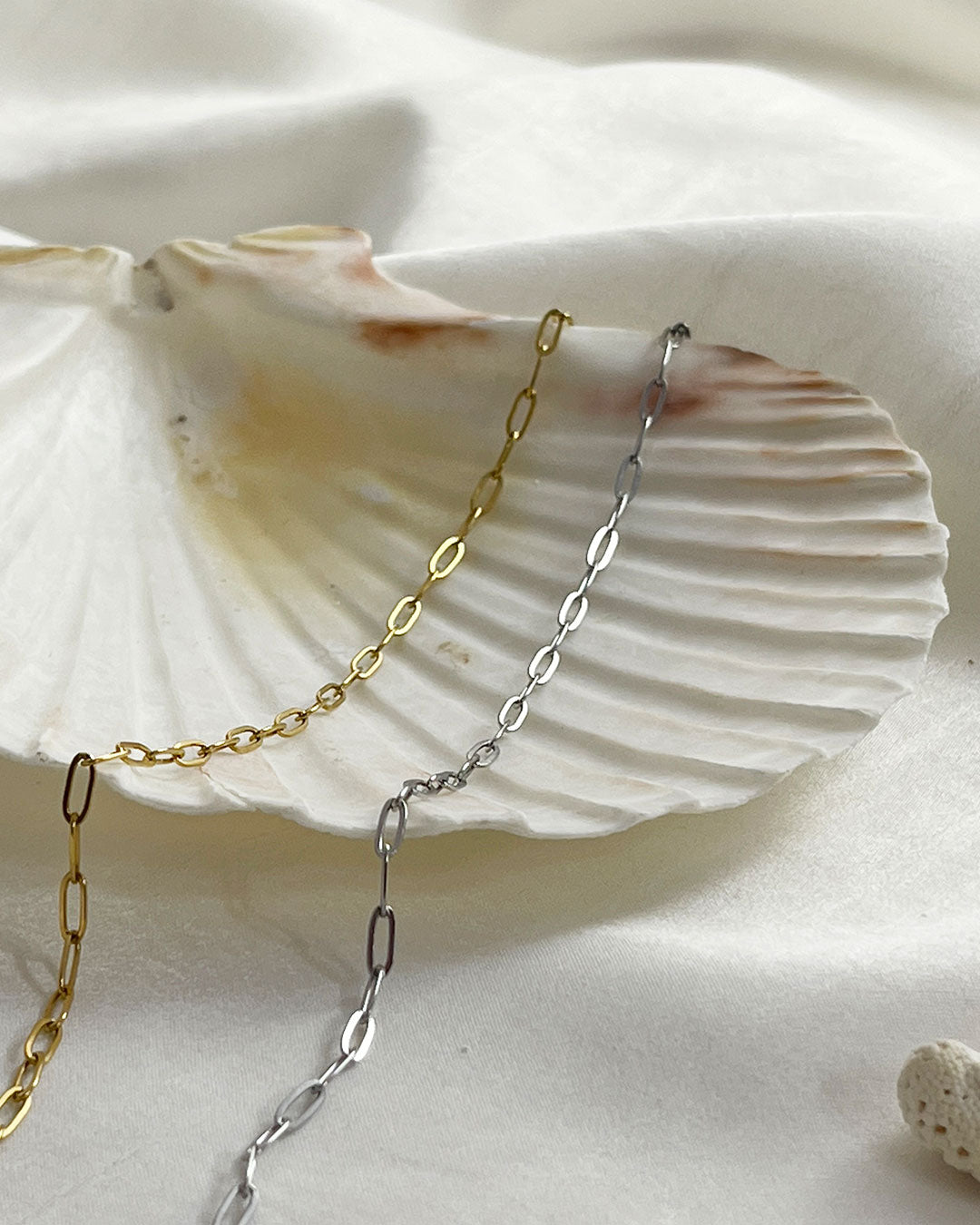 Gold and silver paperclip chain necklaces on a seashell