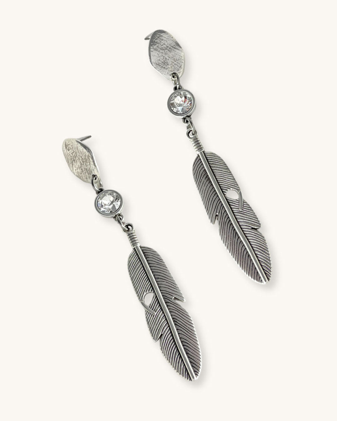 A pair of silver feather earrings with a crystal clear Swarovski. Each earring features a textured silver feather charm dangling from silver oval-shaped studs. The earrings have a bohemian style and are suitable for adding a touch of elegance to any outfit.