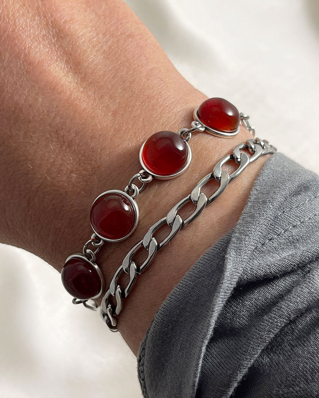 Two silver bracelets stacked: one paperclip chain with carnelian gemstones, and one curb chain bracelet. A modern jewelry set.