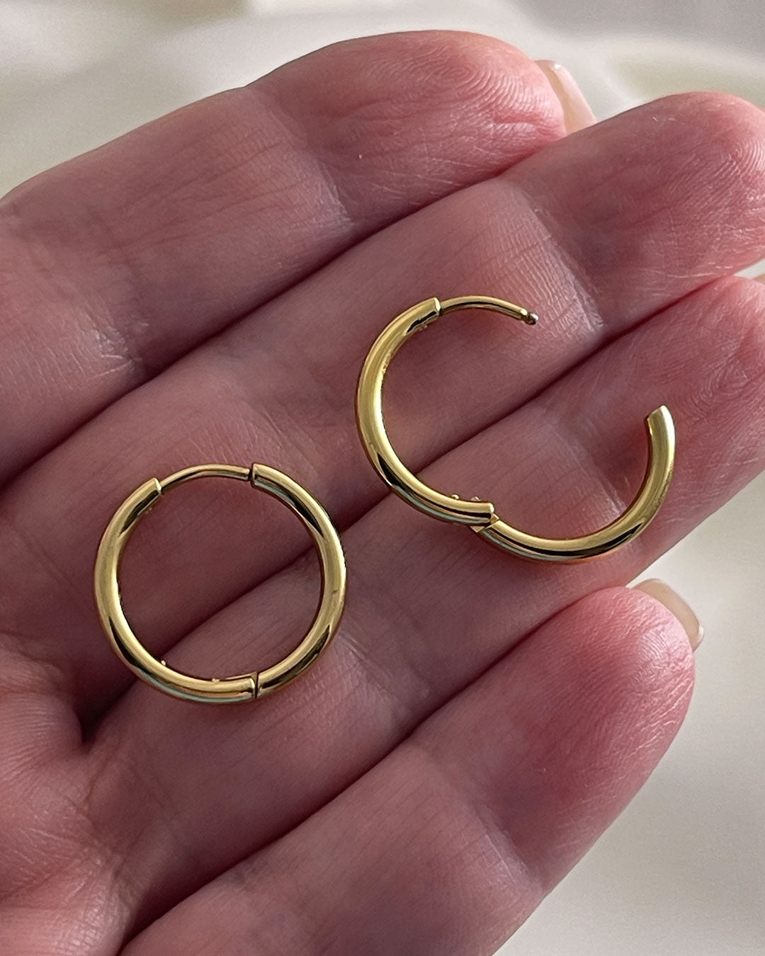 Gold hoop earrings 14mm held between fingers against a neutral background