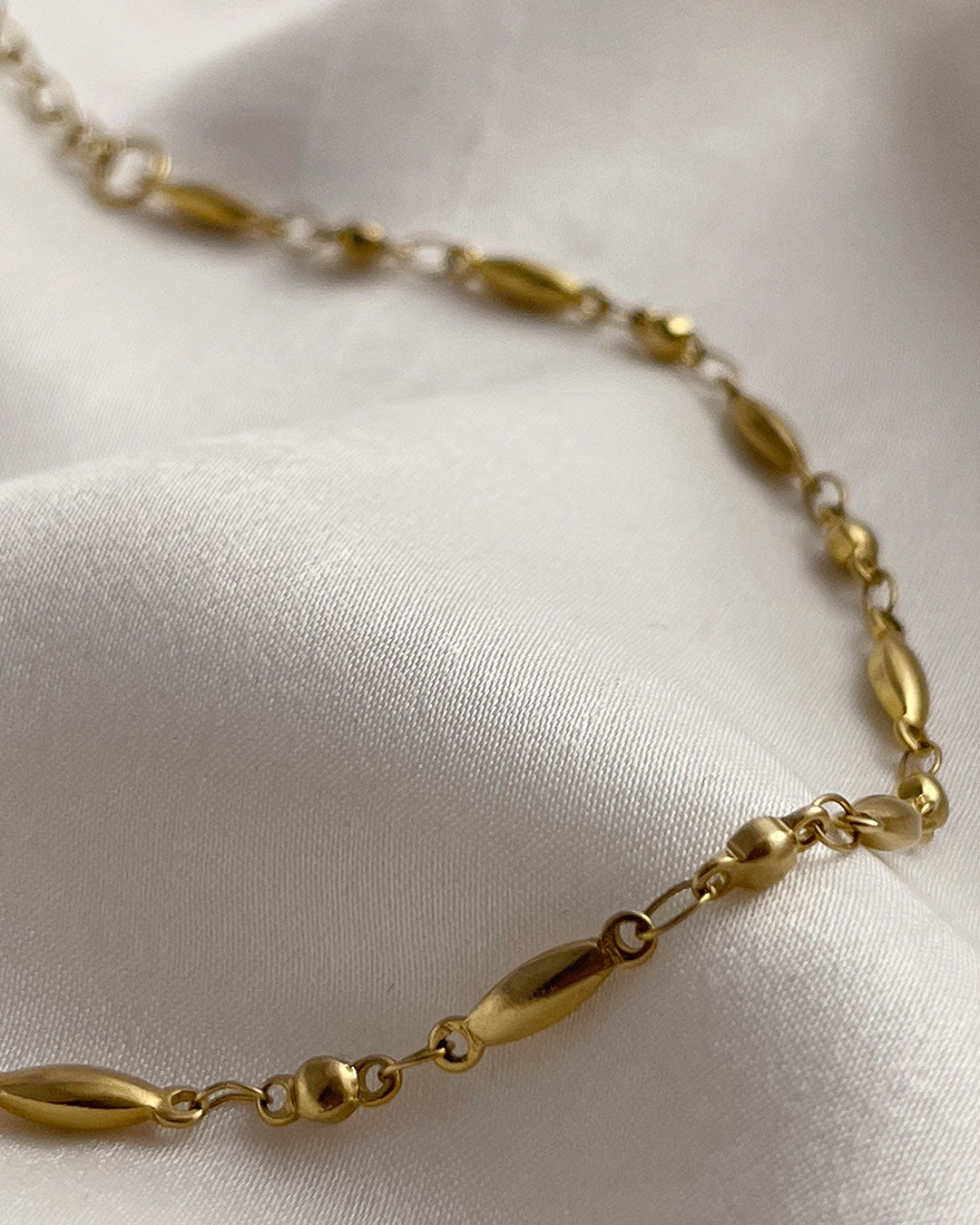 Dainty rice chain bracelet in gold on a white satin surface