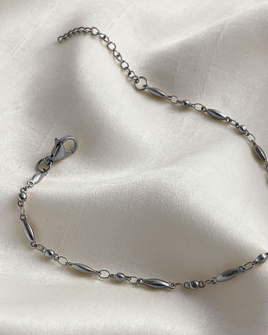 Dainty rice chain bracelet in silver on a white satin surface