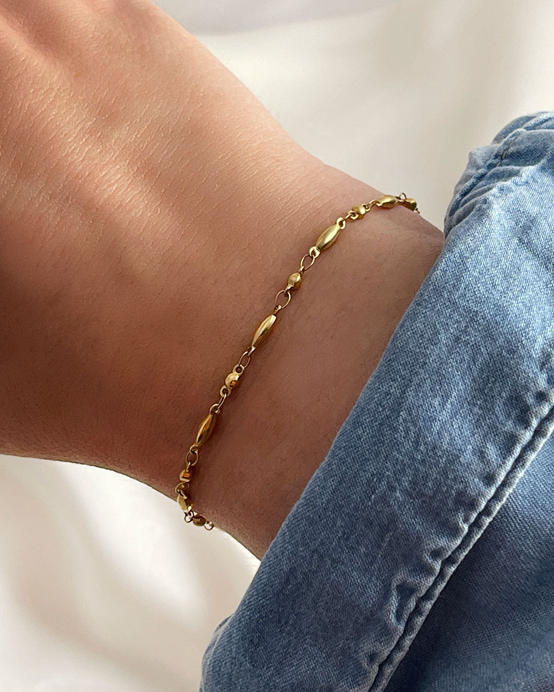 Dainty rice chain bracelet in gold on a wrist with a denim sleeve