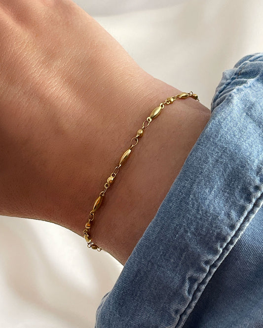 Dainty rice chain bracelet in gold on a wrist with a denim sleeve