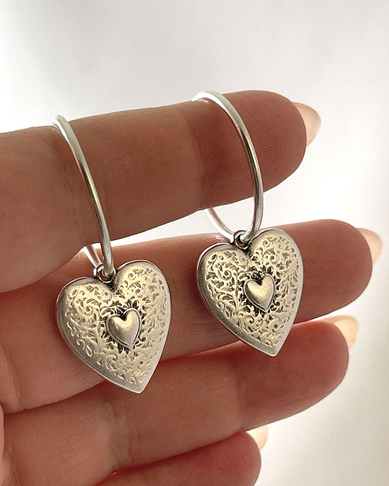The Heart Hoop Earrings, a pair of silver hoop earrings featuring a heart charm.