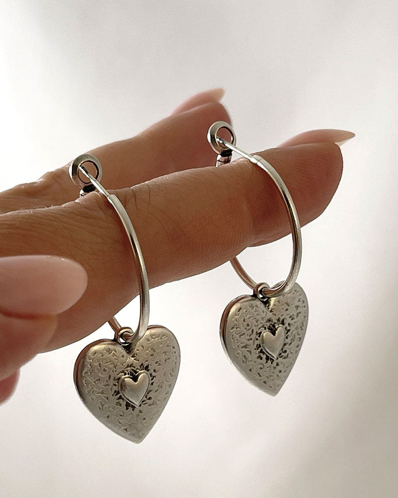 The Heart Hoop Earrings, a pair of silver hoop earrings featuring a heart charm.