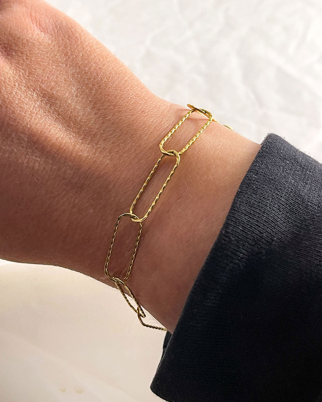 Gold link chain bracelet on a wrist with a neutral background