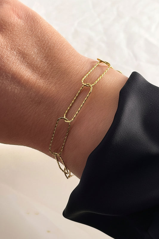Gold link chain bracelet on a wrist with a neutral background