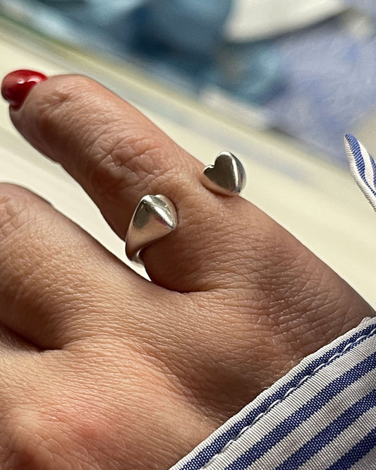 A hand wearing a silver double heart ring.