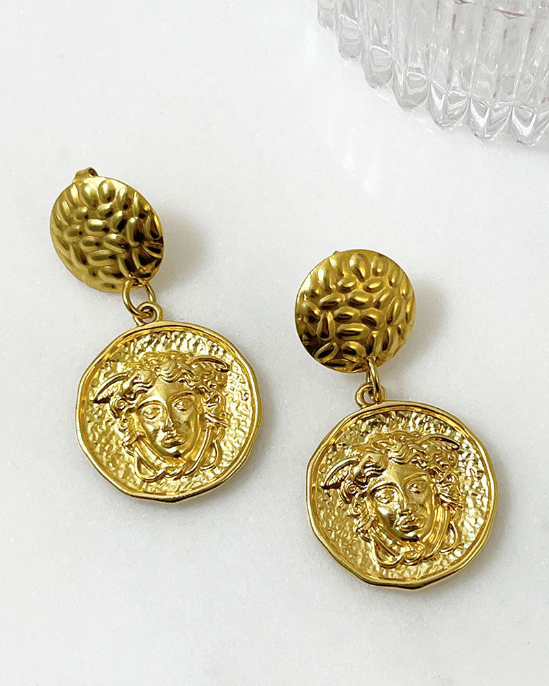 The Medusa Earrings, a pair of gold earrings featuring a round medusa head charm.