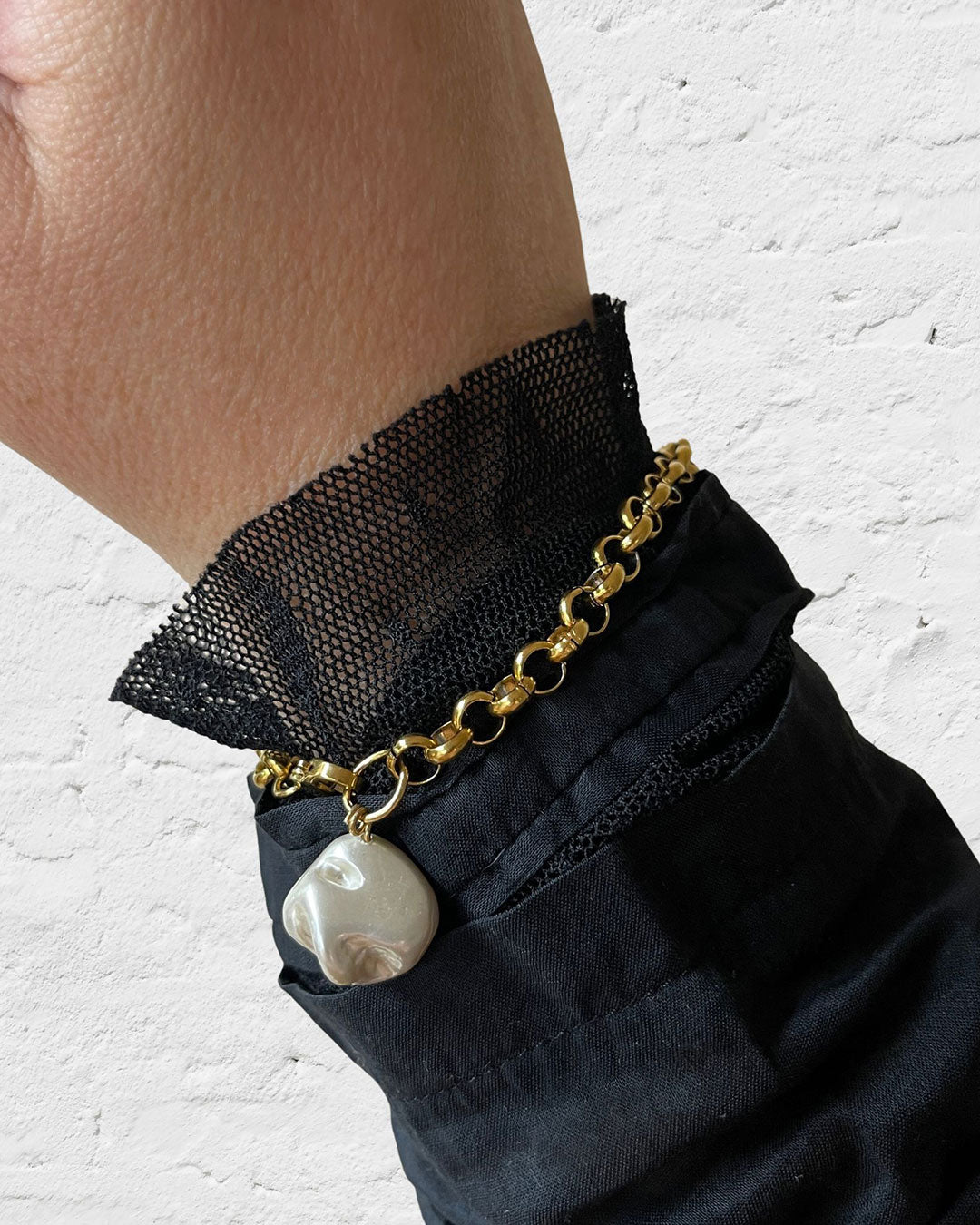 Gold chain bracelet with a MOP shell pearl charm on a wrist against a white background
