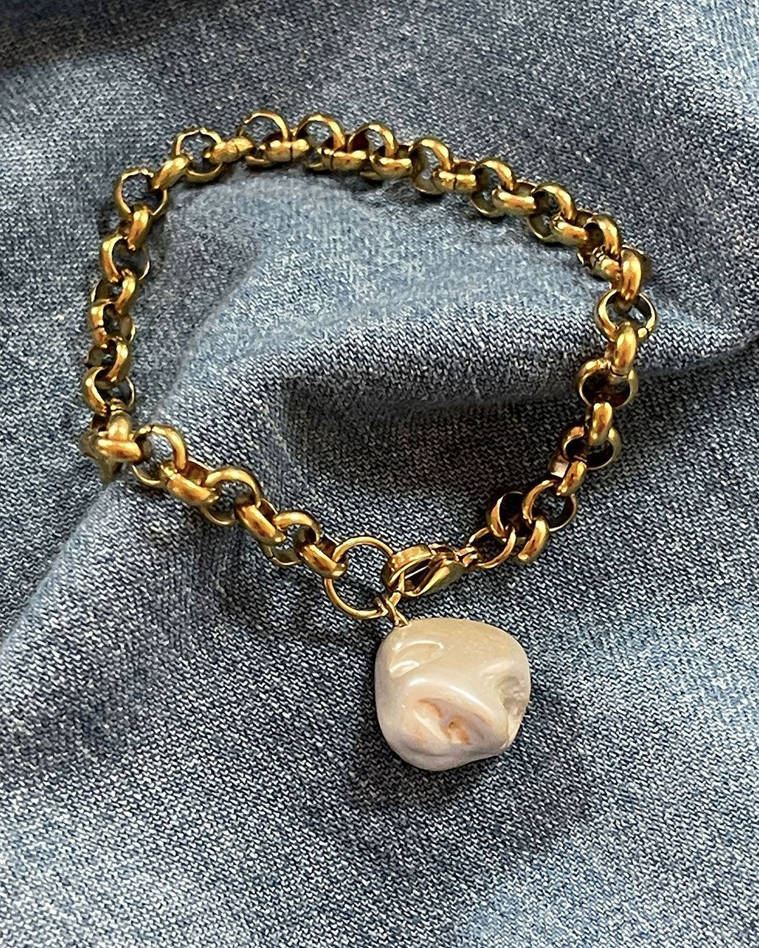 Gold rolo chain bracelet with a MOP shell pearl charm on a denim fabric background