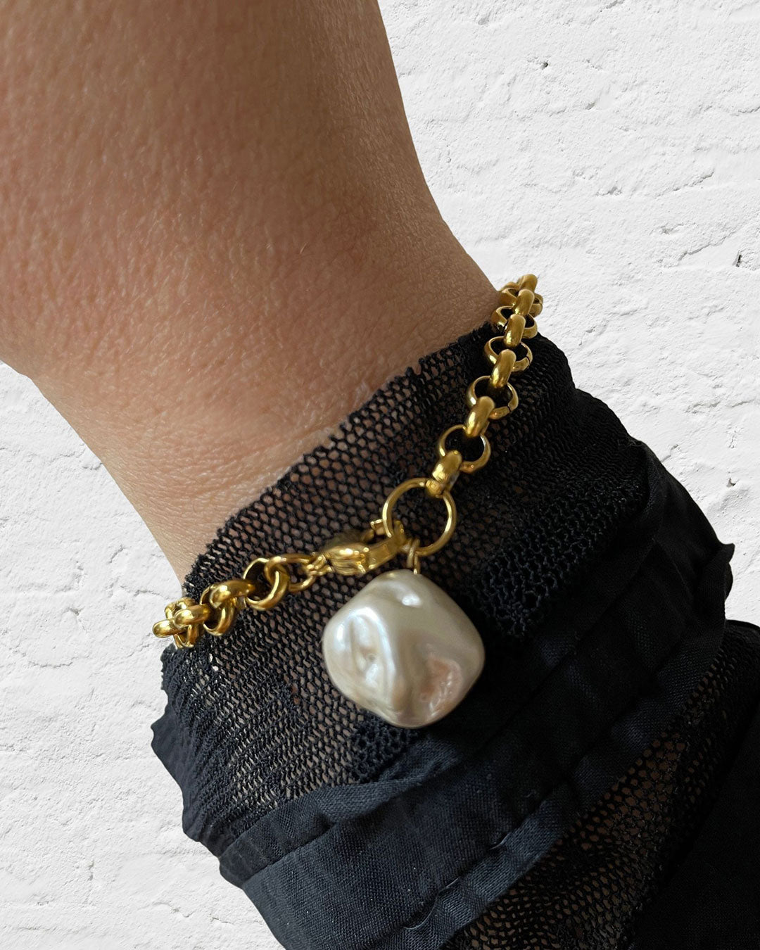 Gold rolo chain bracelet with a large MOP shell pearl charm on a wrist against a white background