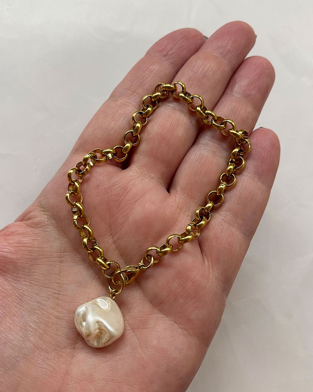 Gold chain bracelet with a MOP shell pearl pendant on a hand against a white background